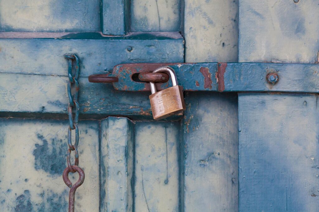 A close-up of a rusty padlock securing a blue painted wooden door with chain and bolt.