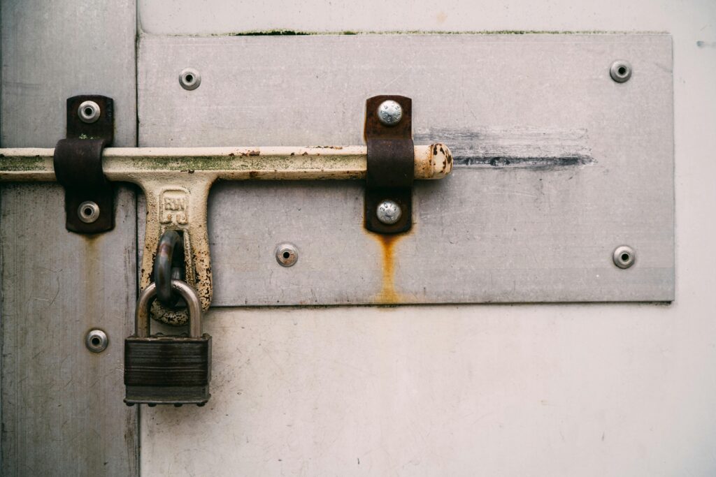 Close-up of a rusty padlock securing a metal door, emphasizing security and protection.